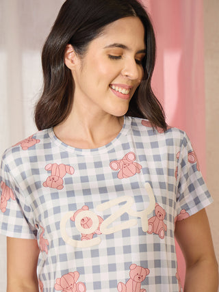 A young woman models a blue and white gingham sleep shirt with an all-over pink teddy bear print and "Cozy" graphic.