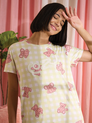 A young woman in a yellow gingham sleep shirt with pink teddy bear print, posing with her hand on her forehead.