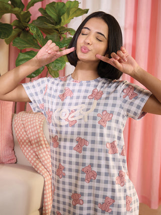 A woman poses playfully in a grey and white checkered sleep dress with pink teddy bear print.