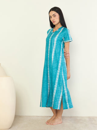 A woman stands with her left side facing the camera, wearing a teal and white tie-dye maxi dress with short sleeves.