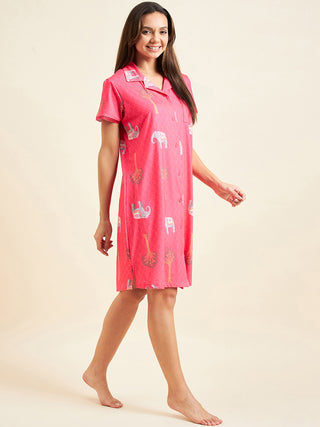 A woman poses in a pink, short-sleeved, collared sleepshirt with an elephant and tree print.