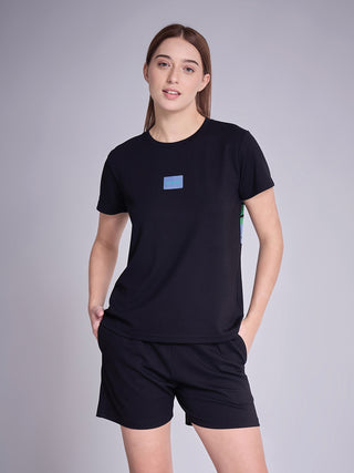A woman poses in a black t-shirt with a blue logo and black shorts.