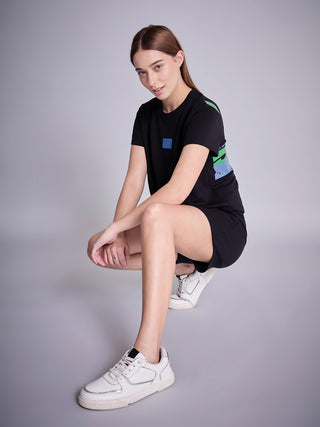A woman crouches, wearing a black t-shirt dress with green and blue abstract print accents.