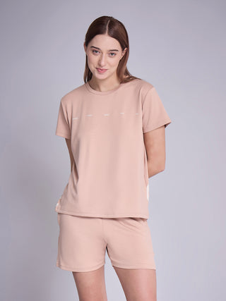 A woman stands posing in a peach-colored t-shirt and shorts with "energy," "happy," "joyful," "love," and "life" printed in white text.