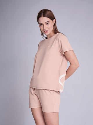 Woman standing in a side pose wearing a warm taupe short-sleeve T-shirt and matching shorts sleepwear set with minimal white word print and side SD graphic.