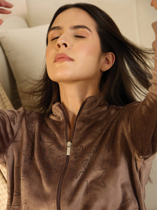 A woman in a brown velour tracksuit with star print, lying down with her eyes closed.