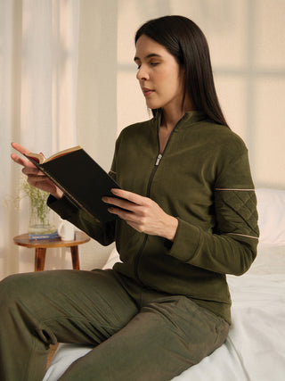 A woman in a green fleece pajama set is reading a book while sitting on a bed.