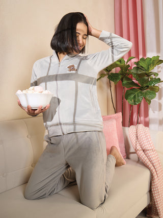 Women, kneeling on a sofa, wearing light gray velour loungewear with a teddy bear print.