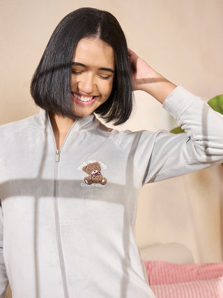 A woman in a grey zip-up sleepwear top with a teddy bear print smiles and touches her hair.
