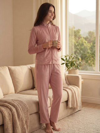 Women in a pink velour pajama set with subtle floral print, standing holding a mug.