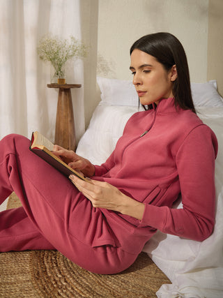 A woman in a pink loungewear set reads a book on the floor.