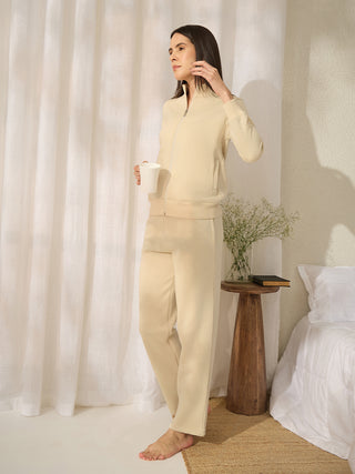 A woman in a cream tracksuit stands holding a mug.