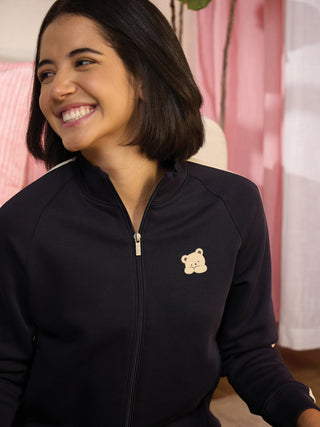 A woman in a dark blue zip-up jacket with a teddy bear print smiles.