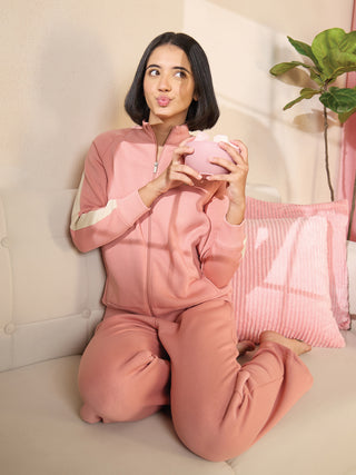 A woman in a pink tracksuit sits on a couch, holding a pink piggy bank.