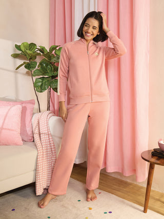 A woman in a pink tracksuit stands with her hand on her head, smiling.
