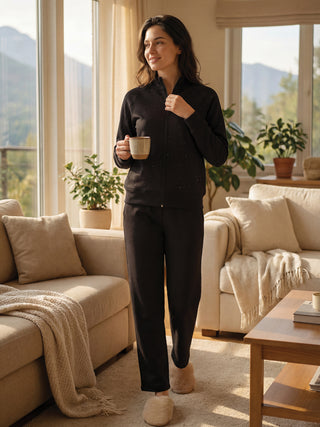 Woman in black printed pajama set and fuzzy slippers, holding a mug.