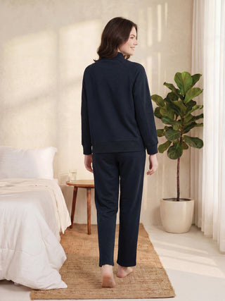 A woman poses from behind in a navy blue tracksuit.