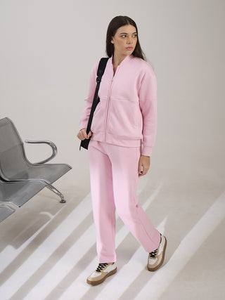 A woman stands posing in a pink tracksuit with a black backpack.