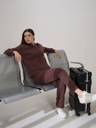 A woman in a maroon loungewear set sits on a bench with a suitcase next to her.