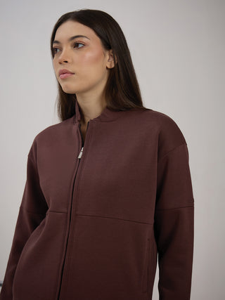 A woman is posing wearing a burgundy zip-up hoodie, the same outfit as the previous image but viewed from a different angle.