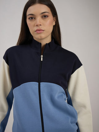 Women in a zipped, color-blocked jacket with navy blue, light blue, and cream panels.