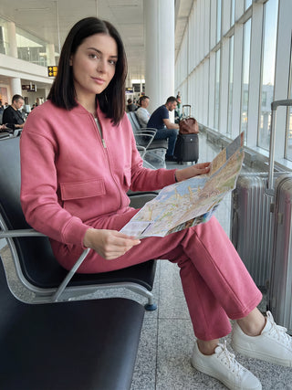 A woman in a pink tracksuit holds a map while sitting in an airport.