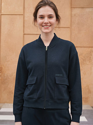 A woman poses in a navy bomber jacket and matching pants.