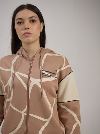 A woman poses wearing a tan and cream giraffe-print zip-up hoodie with a graphic on the left chest, an offering from a sleepwear company.