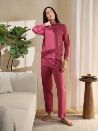 A woman poses in a dusty rose tracksuit with a floral print on the sleeve.