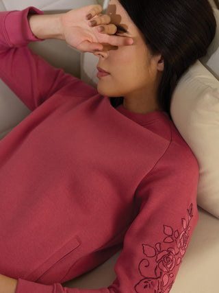 Woman wearing a dusty rose sweatshirt with embroidered roses on the sleeve.