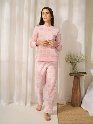 A woman stands holding a glass, wearing pink patterned pajamas.