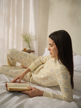 A woman is lying on a bed wearing a yellow pajama set with a floral print.