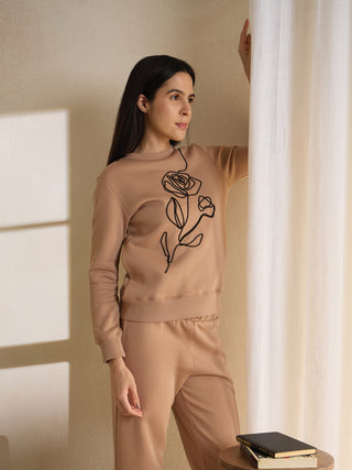 Woman posing by a curtain wearing a tan loungewear set with a minimalist rose print.