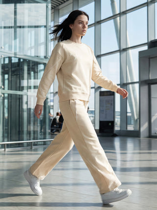 A woman in a cream-colored sweat suit with a star print walks through a modern airport terminal.