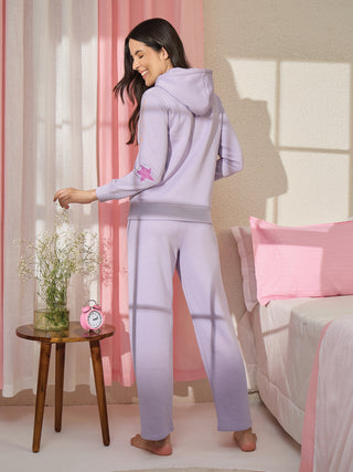 A woman poses wearing a light purple hooded sweatshirt and matching sweatpants, featuring star prints.