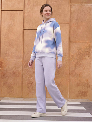 A young woman poses in a tie-dye hoodie and matching lavender sweatpants, standing on a crosswalk.