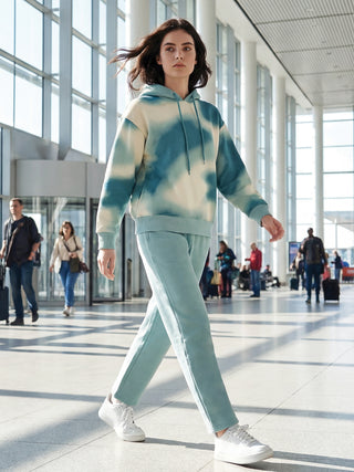 A woman is walking in an airport wearing a tie-dye print hoodie and matching sweatpants.