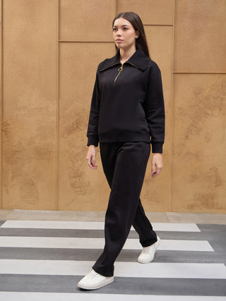 A woman walks across a zebra crossing wearing a black quarter-zip sweatshirt and matching black sweatpants.