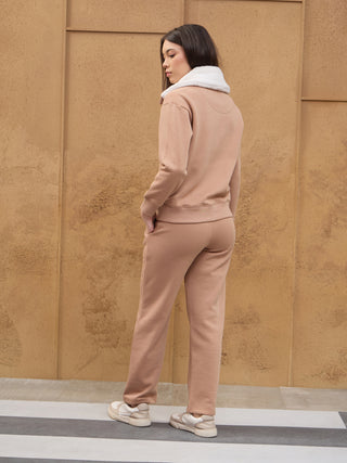 A woman stands facing away from the camera, wearing a tan loungewear set with a white fuzzy collar.