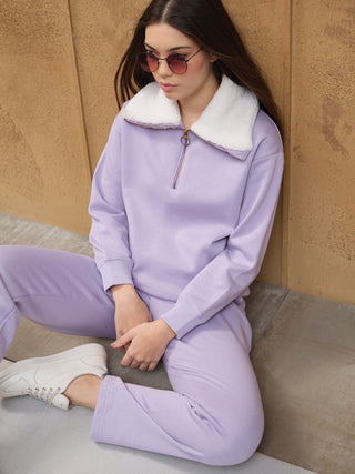 A young woman in a lilac quarter-zip sweatshirt with a white fur collar and matching sweatpants.