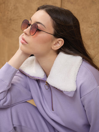 Woman wearing a light purple sweatshirt with a white fuzzy collar, with her hand on her chin.