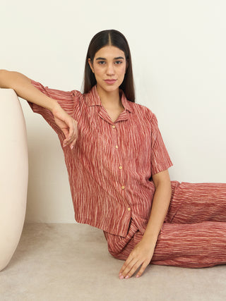 A woman poses seated, wearing a red striped pajama set.
