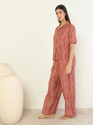 A woman stands in a brick-red, striped, pleated pajama set.