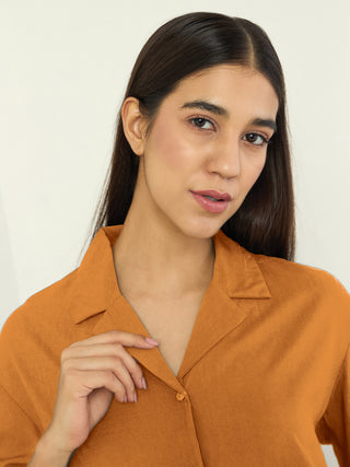 Woman in an orange collared shirt, posing and gently touching her collar.