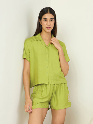 A woman in a lime green pajama set with floral embroidery poses confidently, standing against a white wall.