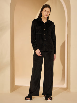 Women in a black velvet pajama set consisting of a collared button-down shirt and wide-leg pants, standing and looking at the camera.