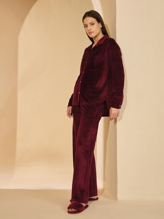 Woman wearing burgundy velvet pajamas and slippers, leaning against a wall.