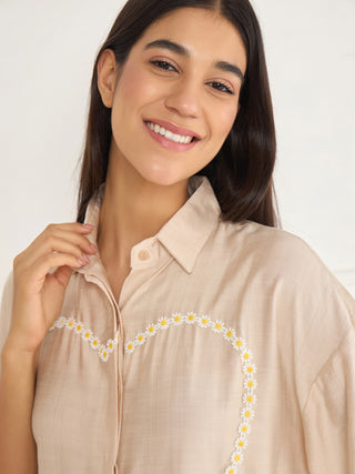 A woman poses wearing a light beige collared pajama top with a heart-shaped daisy print.