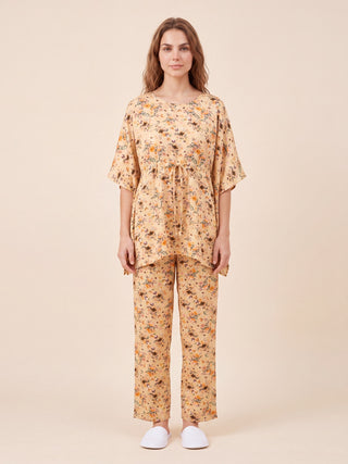 A woman stands facing forward wearing a peach floral print pajama set with white slippers.