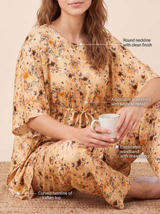A woman in a peach floral print silk kaftan pajama set, sitting with a mug of coffee.